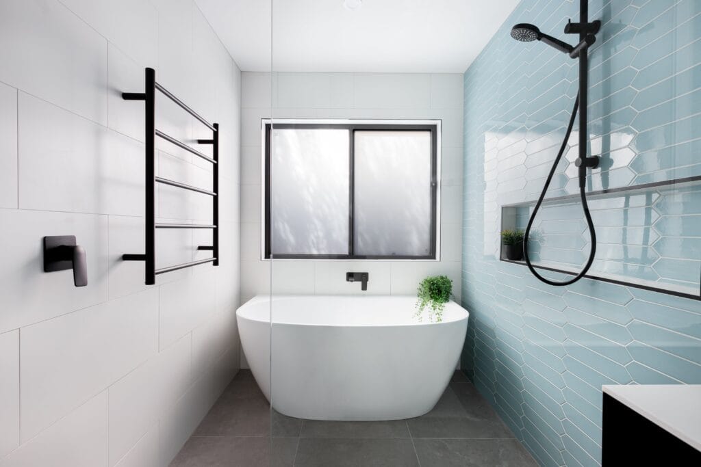 Modern bathroom with a freestanding bathtub, frosted window, black fixtures, blue tiled shower wall, and a heated towel rail.