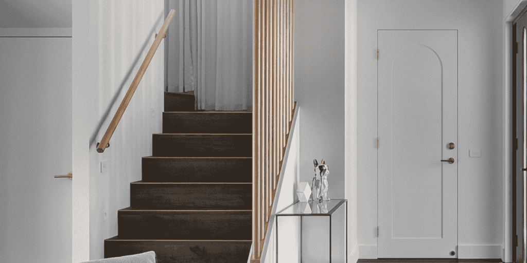 Modern entryway with dark wood stairs, white walls, a glass console table, and an arched white door.